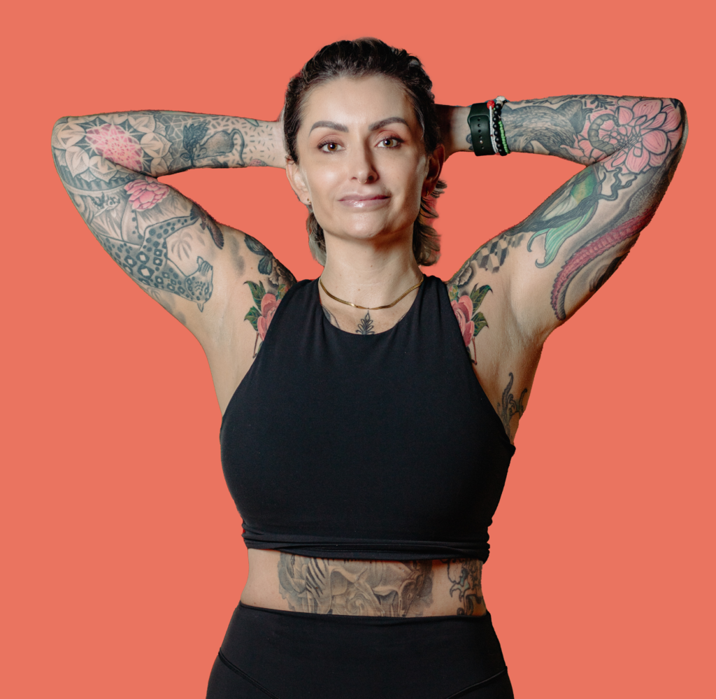 Koltie profile picture. She has hands behind her head, lots of tattoos with an orange background. Chandra Vida retreats.