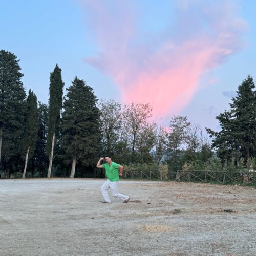 Carlito does a muscle pose with a pink and glorious sunset at the polo club in Tuscany. Chandra Vida Retreats.