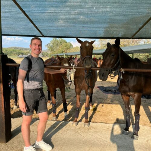 Charlie poses in front of the polo ponies at the polo club in tuscany. Chandra Vida Retreats.